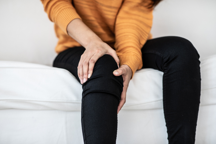 Photo of woman holding her knee experiencing pain behind the knee and calf area
