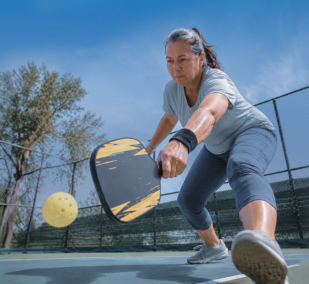 Woman on an outdoor pickleball court lunging for the ball with her paddle