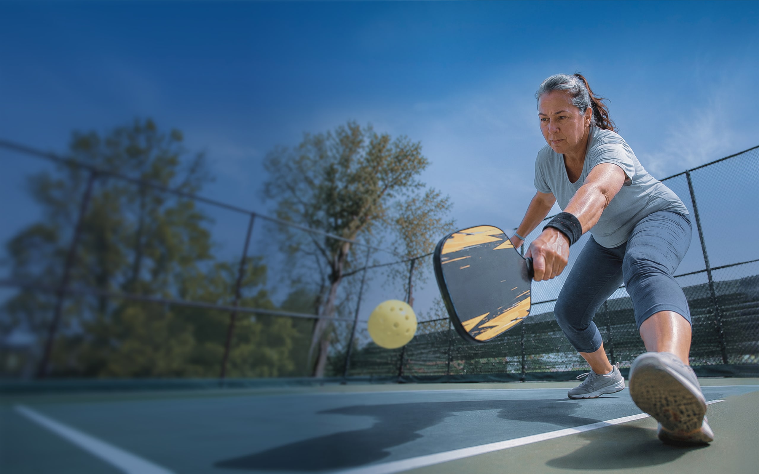 Woman on an outdoor pickleball court lunging for the ball with her paddle