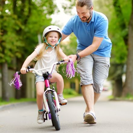 father helping daughter learn to ride bike