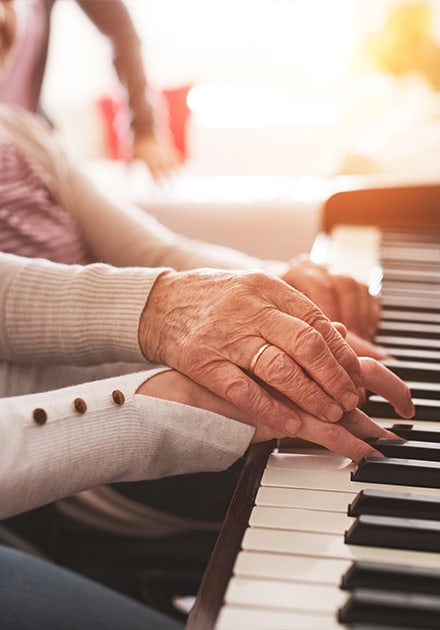 close-up of the hands of an elderly woman and young woman playing piano