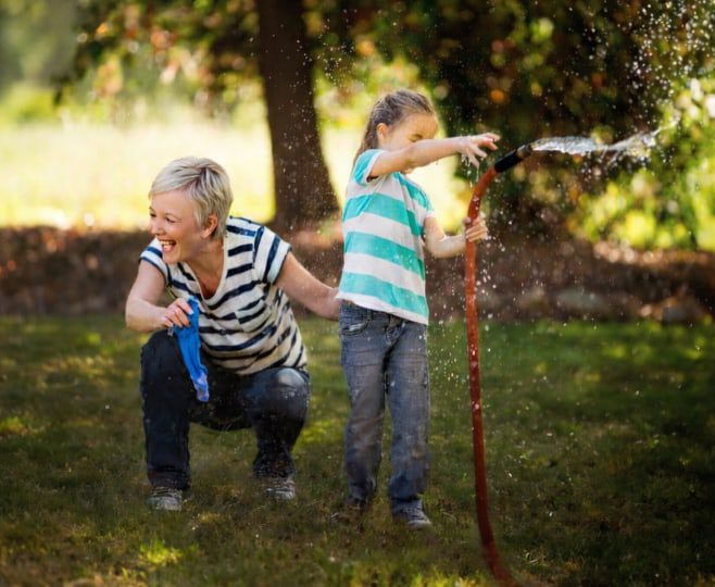 Grandmother playing with her granddaughter with the sprinkler