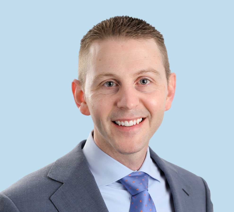 Dr. Christopher Reb wearing a grey suit and blue tie.