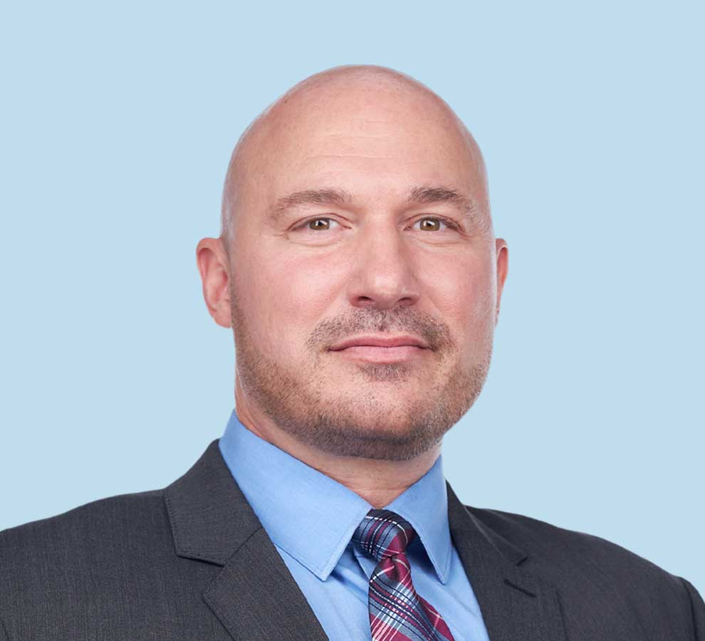 Thomas S. Stang, DO professional headshot wearing black suit and plaid red tie
