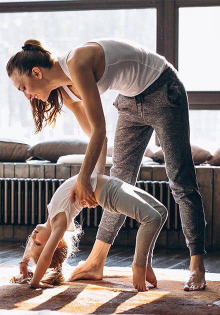 Mother helping young daughter do yoga